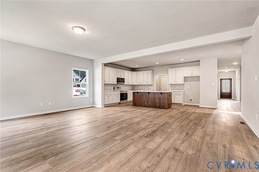 Open-concept living space featuring wood-finish flooring, recessed lighting, a kitchen with white cabinetry, a dark wood-finish island, and a dark front entry door