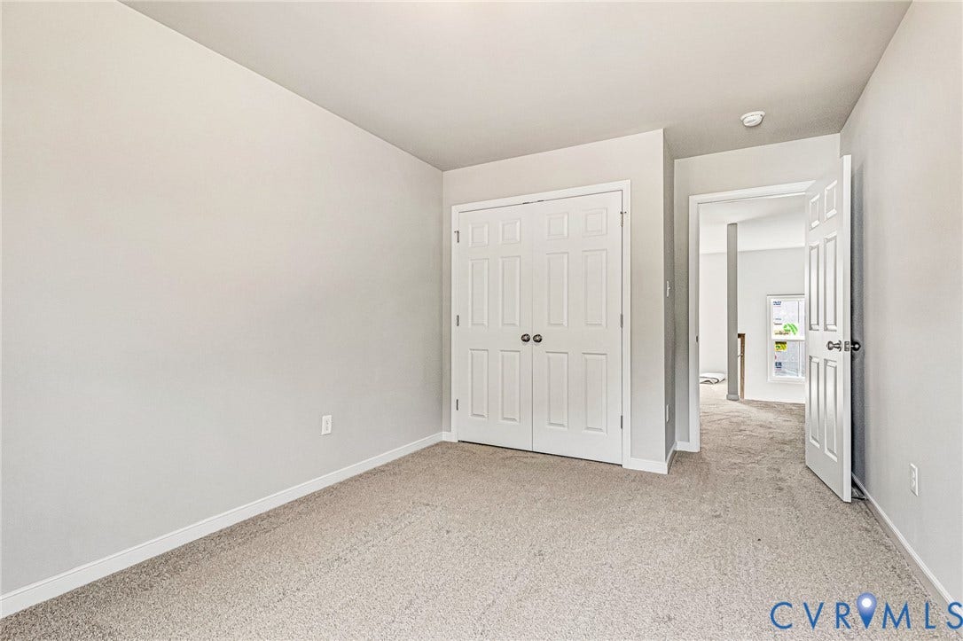 Carpeted room featuring light gray walls, white trim, and a white bi-fold closet door