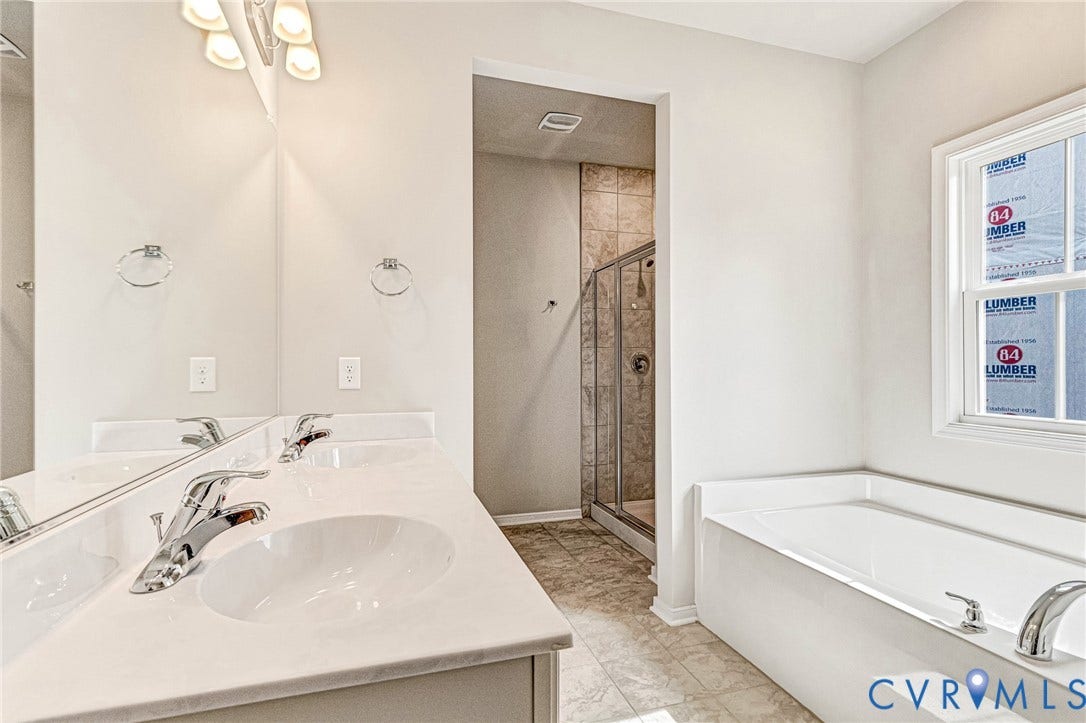 Bathroom featuring a dual vanity with white countertops, chrome fixtures, an enclosed shower with tiled walls, a separate soaking tub, and tile flooring