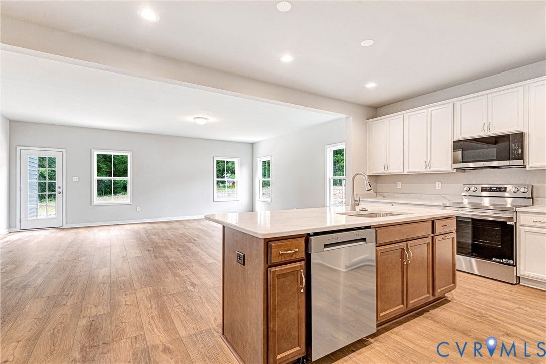Modern kitchen featuring white upper cabinetry, a central island with wood-finish base cabinets and an undermount sink, stainless steel appliances, and wood-finish flooring extending into the adjacent living area