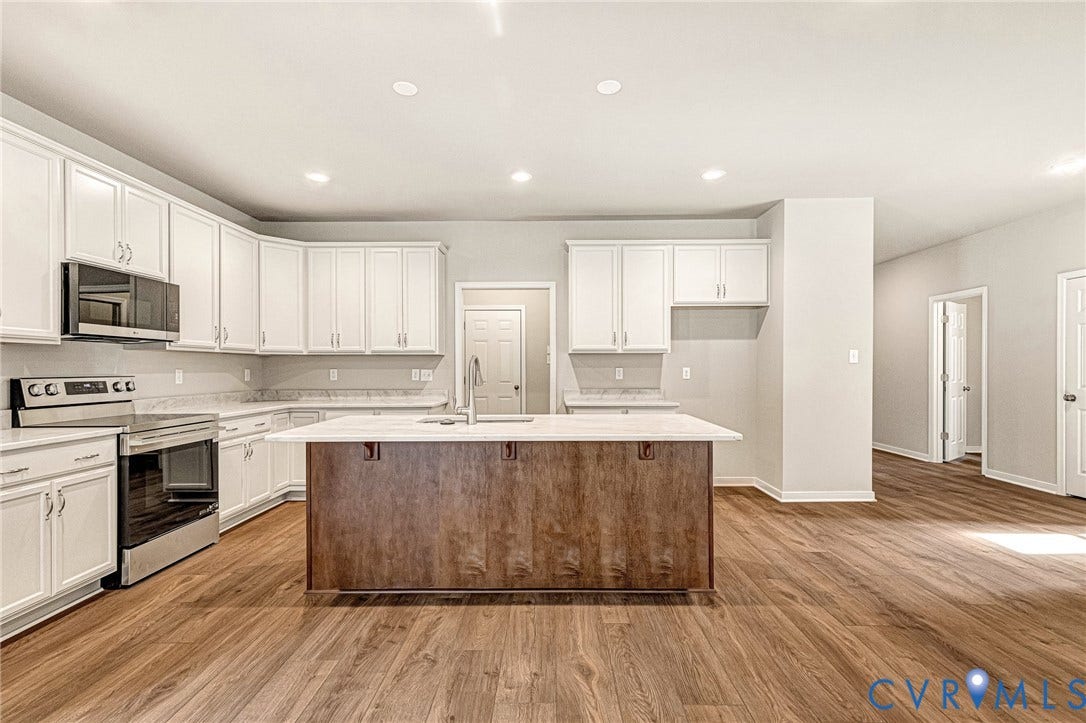 Contemporary kitchen with wood-finish flooring, white cabinetry, stainless steel appliances, a center island with contrasting wood-finish base, and recessed lighting