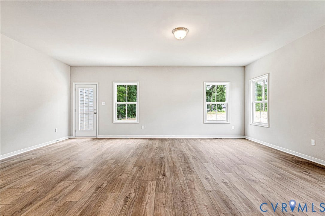 Spacious interior featuring wood-finish flooring, light gray walls, white trim, and multiple windows