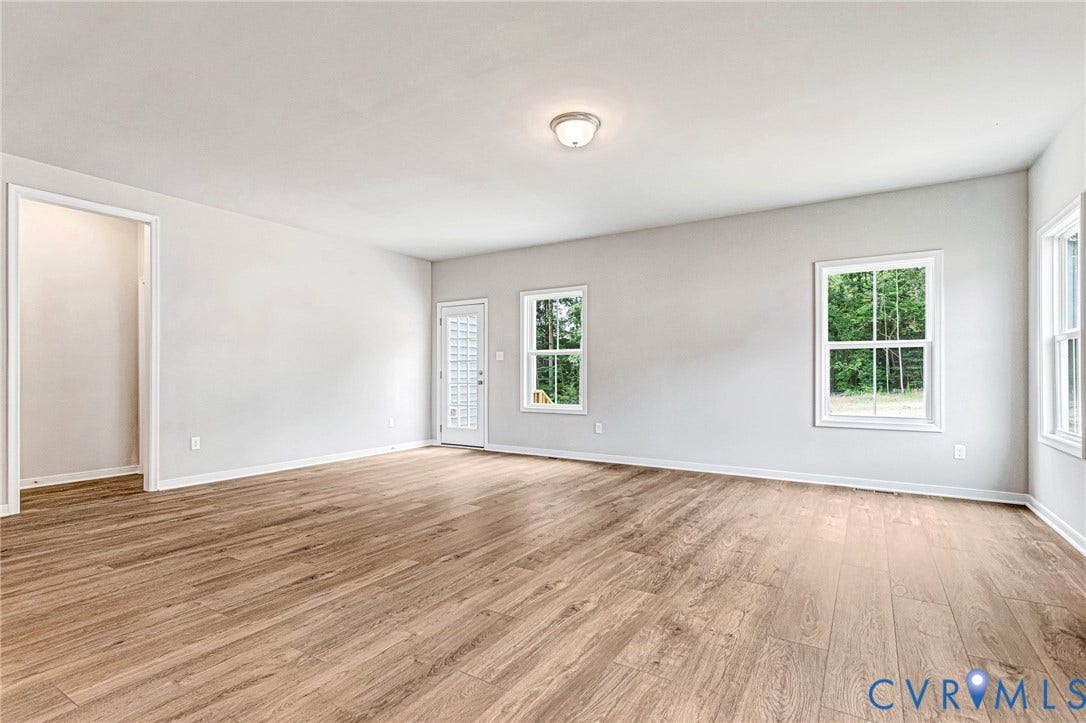 Spacious room featuring wood-finish flooring, light grey walls, white trim, and multiple windows