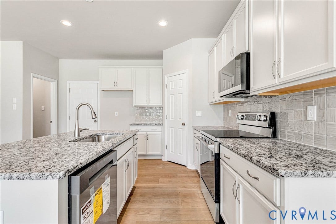 12606 Poplar Village Place, Poplar Village, Chester, VA 23831 Kitchen featuring a center island with undermount sink and gooseneck faucet, light wood-finish flooring, white cabinetry, integrated stainless steel appliances, and a tiled backsplash