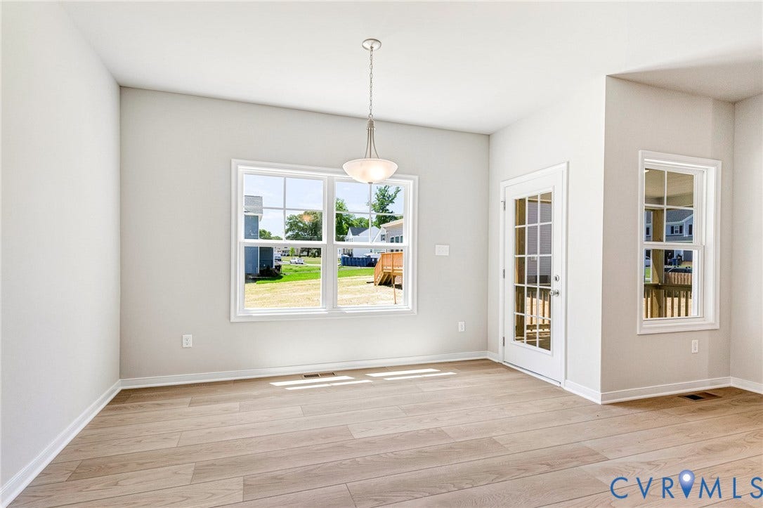 12606 Poplar Village Place, Poplar Village, Chester, VA 23831 Bright interior space featuring light wood-finish flooring, a white trim window overlooking a green yard, a glass-paneled door leading to an outdoor deck, and a contemporary pendant light fixture