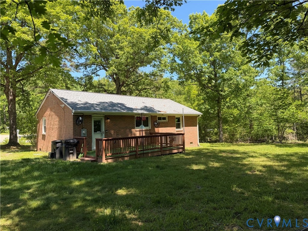 1611 Anderson Highway, Powhatan, VA 23139 Brick ranch-style home featuring a grey shingle roof, a wooden ramp leading to a rear deck, and a large grassy yard bordered by mature trees
