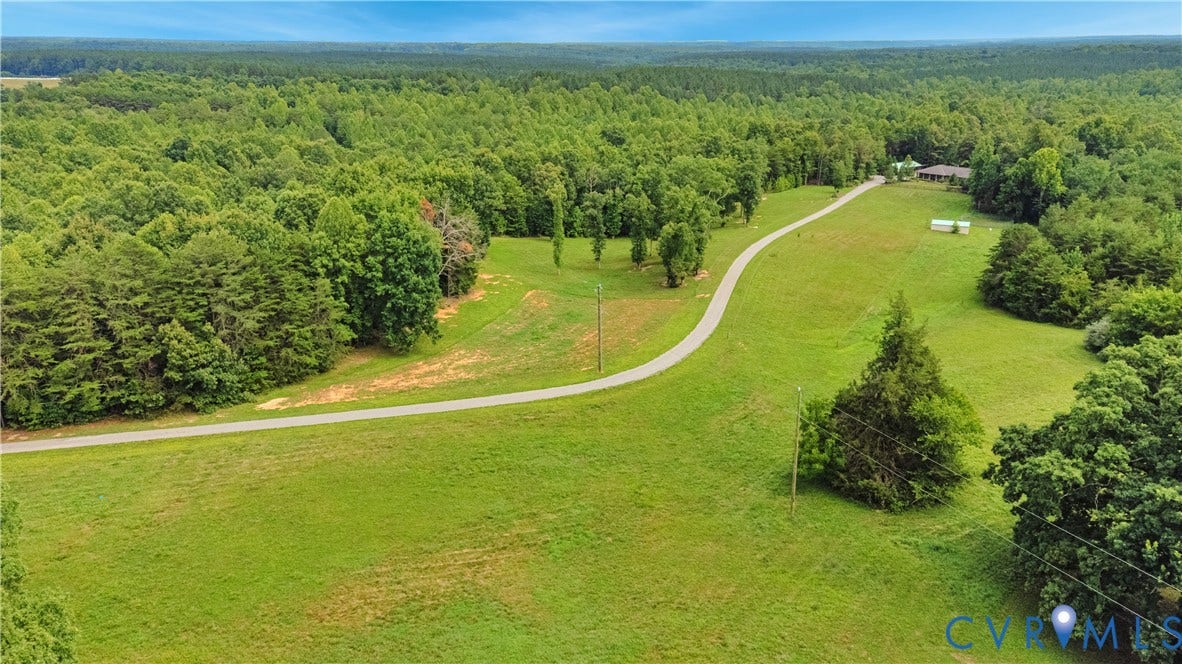4337 Riddles Bridge Road, Riddles Bridge, Goochland, VA 23063 Expansive property featuring a paved driveway, a structure with a brown roof, and a backdrop of dense woodland