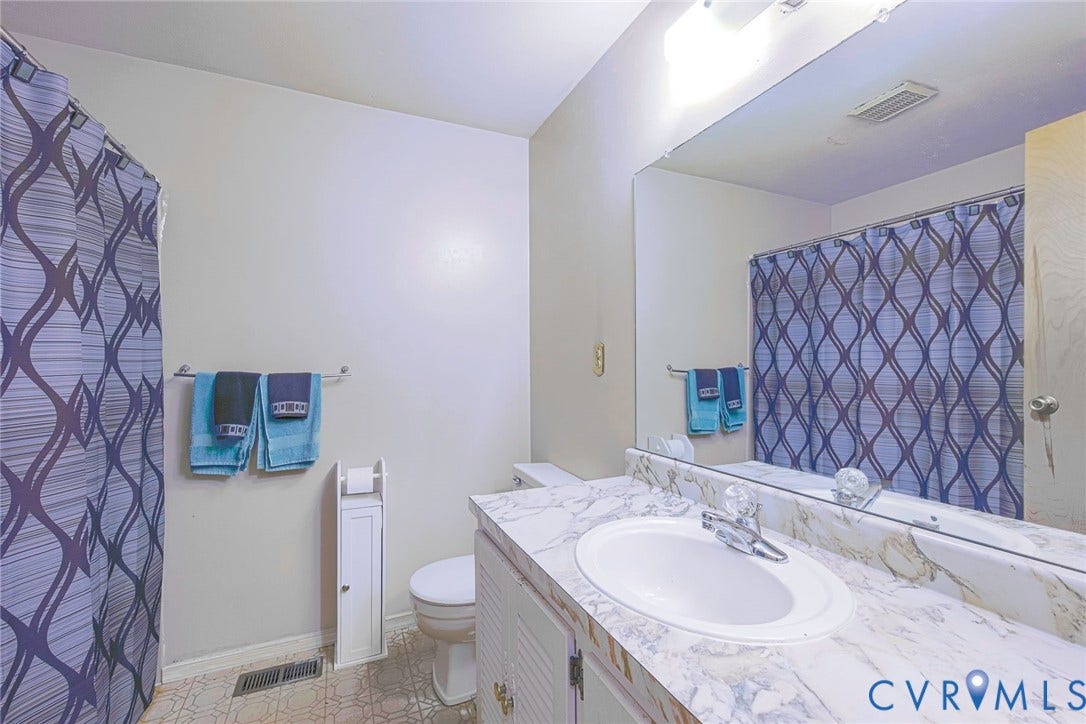 The bathroom features a vanity with a countertop and an integrated sink, a toilet, and a shower area with a patterned curtain