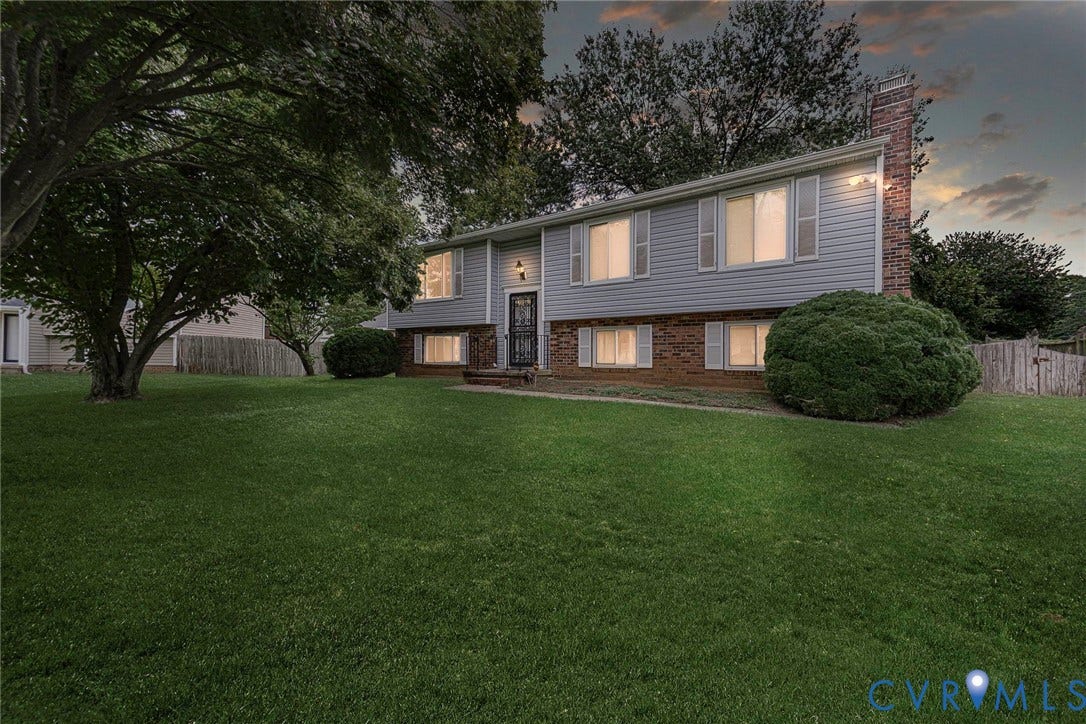 Split-level residence featuring a brick and siding exterior, front lawn, mature tree, and a prominent brick chimney