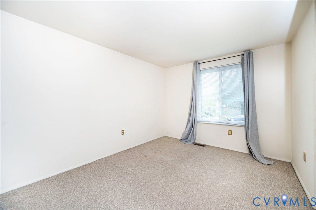 Carpeted room with a double-pane window, neutral wall tones, and a baseboard vent