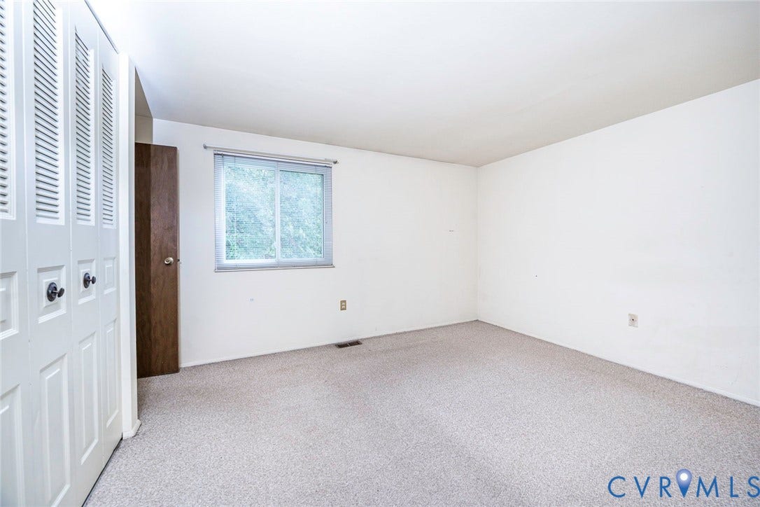 Carpeted interior space with a window, white walls, and a louvered bi-fold closet door