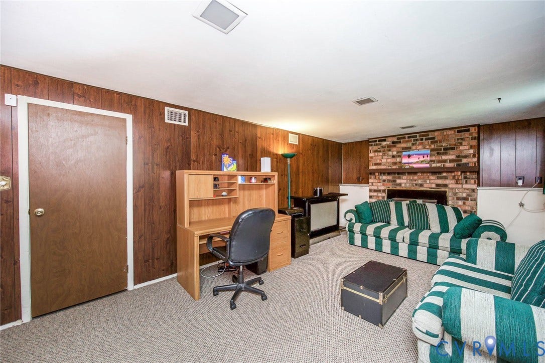 Spacious living area featuring paneled walls, a brick fireplace, and carpet flooring