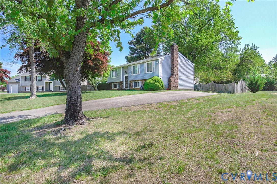 This property features a spacious yard with a paved driveway, mature trees, and a wooden fence