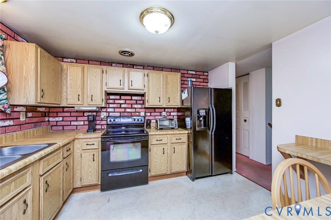 Well-appointed kitchen featuring wood cabinetry, a double basin sink, black appliances including a refrigerator and range, and a brick-patterned backsplash