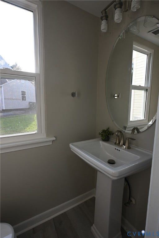 912 Harmony Road, Fairfield, VA 23059 Pedestal sink with a brushed nickel faucet, large oval mirror, and wood-finish flooring