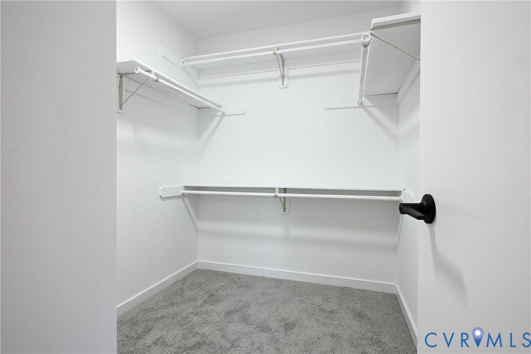 912 Harmony Road, Fairfield, VA 23059 Spacious walk-in closet featuring multiple shelving units, a hanging rod with black end cap, and neutral carpeted flooringideal for organized storage and wardrobe display