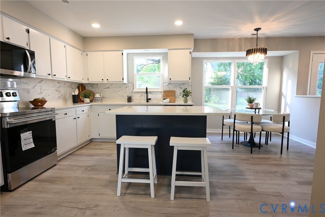 912 Harmony Road, Fairfield, VA 23059 White cabinetry with black hardware, stainless steel appliances, patterned backsplash, center island with an extended countertop, and wood-finish flooring