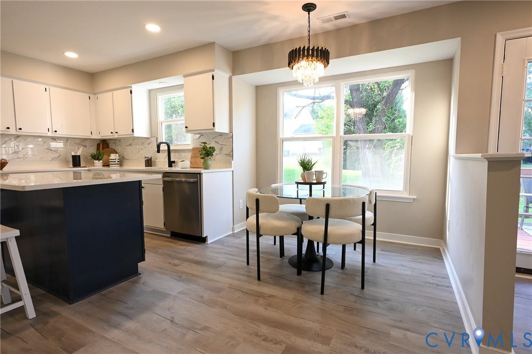 912 Harmony Road, Fairfield, VA 23059 Open-concept kitchen and dining area featuring white cabinetry with stainless steel appliances, quartz countertops, a black-finished kitchen island, wood-finish flooring throughout, large multi-pane windows with natural light, and a modern pendant light fixture