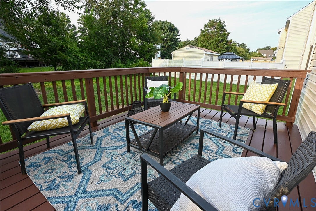 912 Harmony Road, Fairfield, VA 23059 Elevated composite deck featuring rich wood-finish railings, integrated seating areas with cushioned chairs, a dark metal fire table with glass top, and a geometric patterned outdoor rug