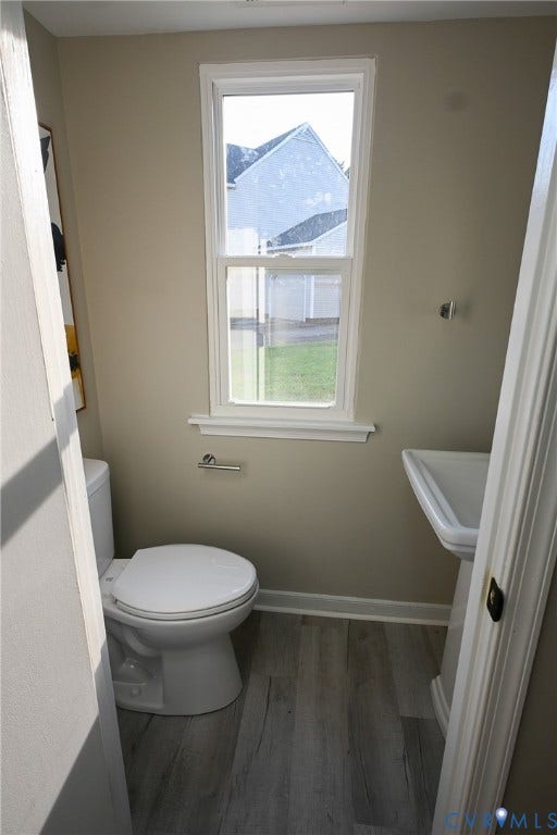 912 Harmony Road, Fairfield, VA 23059 Compact half bath featuring a ceramic toilet, wood-finish flooring, neutral wall finishes, and a large single-hung window with white trim providing natural light and outdoor visibility