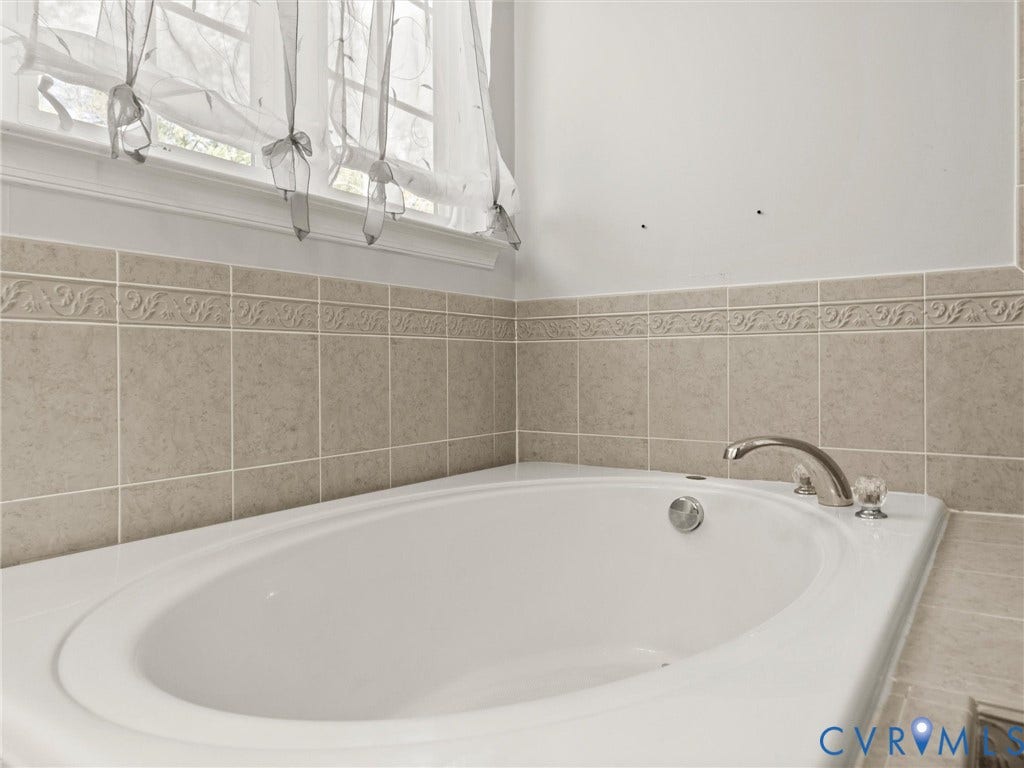 126 Reedy Creek Road, Reedy Creek, Louisa, VA 23093 Soaking tub with chrome fixtures, surrounded by beige tiled walls featuring a decorative trim