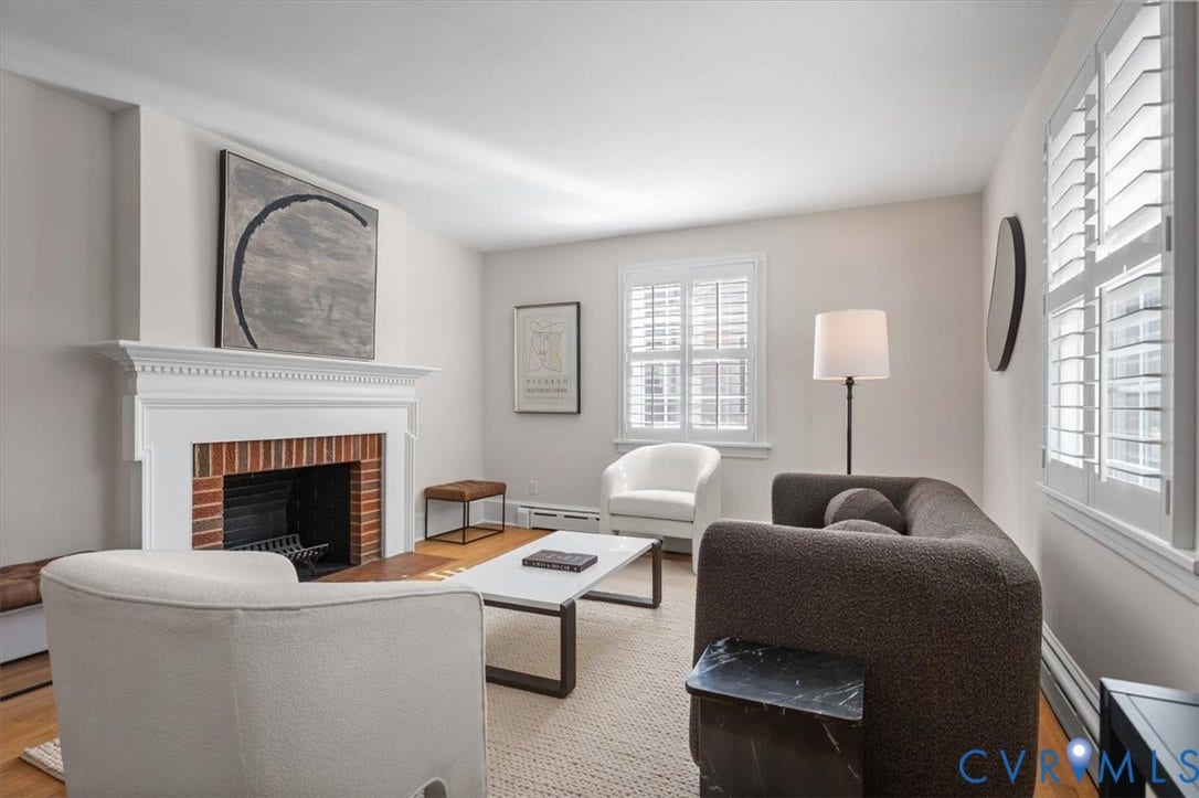 613 Maple Avenue, Near West End, Richmond, VA 23226 Brick fireplace with a substantial white mantel, multiple windows with white plantation shutters, light-toned walls, and wood-finish flooring