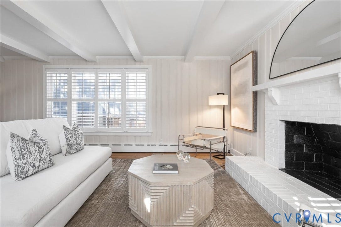 613 Maple Avenue, Near West End, Richmond, VA 23226 Exposed ceiling beams, white brick fireplace with black firebox, wood-finish flooring, white panel wall finishes, and plantation shutters