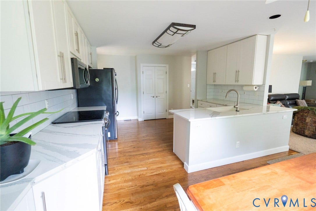 1670 Mill Quarter Road, Powhatan, VA 23139 Bright, open-concept kitchen featuring white cabinetry, a large waterfall-edge island with seating, stainless steel appliances, and wood-finish flooring throughout
