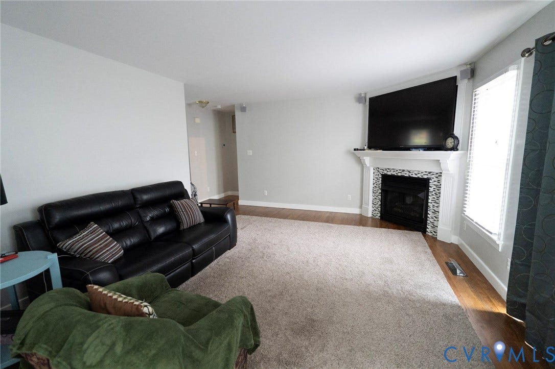 1670 Mill Quarter Road, Powhatan, VA 23139 Spacious living room featuring a fireplace with decorative surround, wall-mounted flat-screen television, carpeted flooring, and abundant natural light from multiple windows