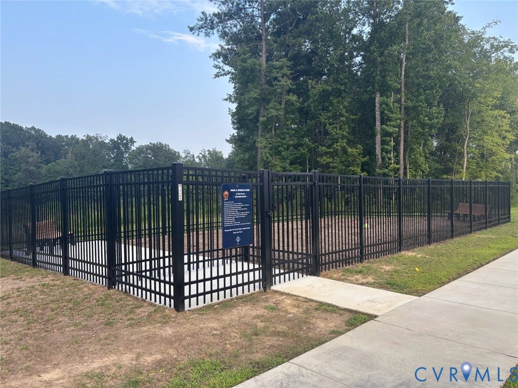 7236 George Wythe Lane, Summer Maple, New Kent, VA 23124 Fenced pet area featuring a dark metal fence, concrete entrance, and natural ground cover