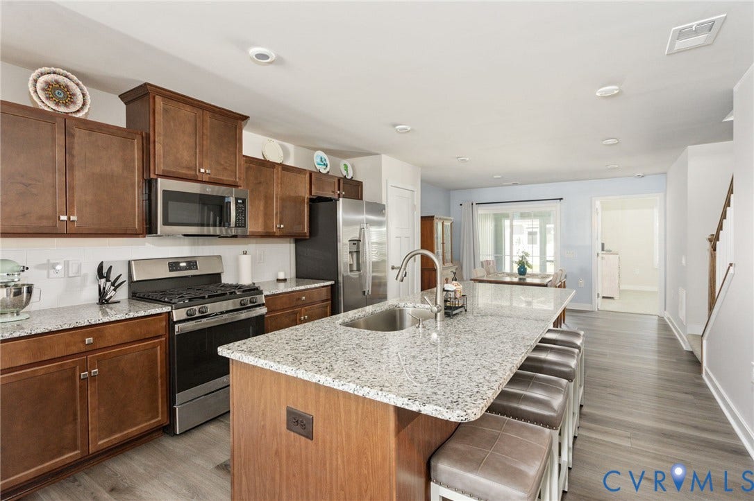 7236 George Wythe Lane, Summer Maple, New Kent, VA 23124 Kitchen featuring a large island with a stainless steel sink, wood-finish flooring, stainless steel appliances, brown cabinetry, and light-toned countertops