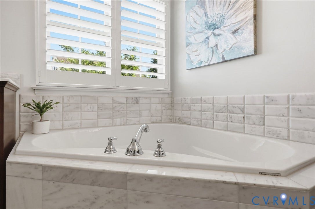 4909 Parsons Walk Place, Twin Hickory, Glen Allen, VA 23059 Corner soaking tub featuring chrome fixtures, surrounded by white stone-finish tile and a white wood shuttered window