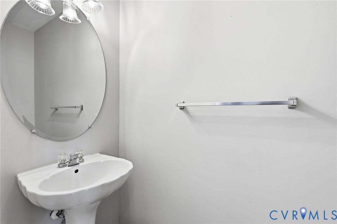 White pedestal sink with chrome faucet, an oval mirror, and a three-light vanity fixture