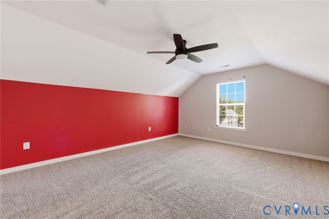 Spacious room featuring vaulted ceilings, a ceiling fan, a window with blinds, and neutral carpeting
