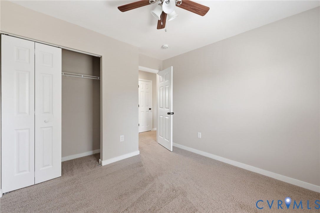 Carpeted interior room featuring neutral wall paint, white trim, and a ceiling fan with light fixture