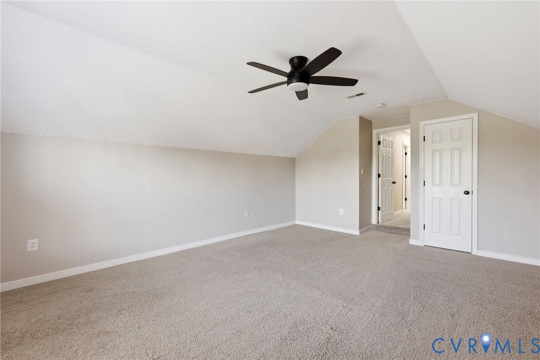 Spacious attic room featuring sloped ceilings, light neutral wall tones, and plush carpet flooring