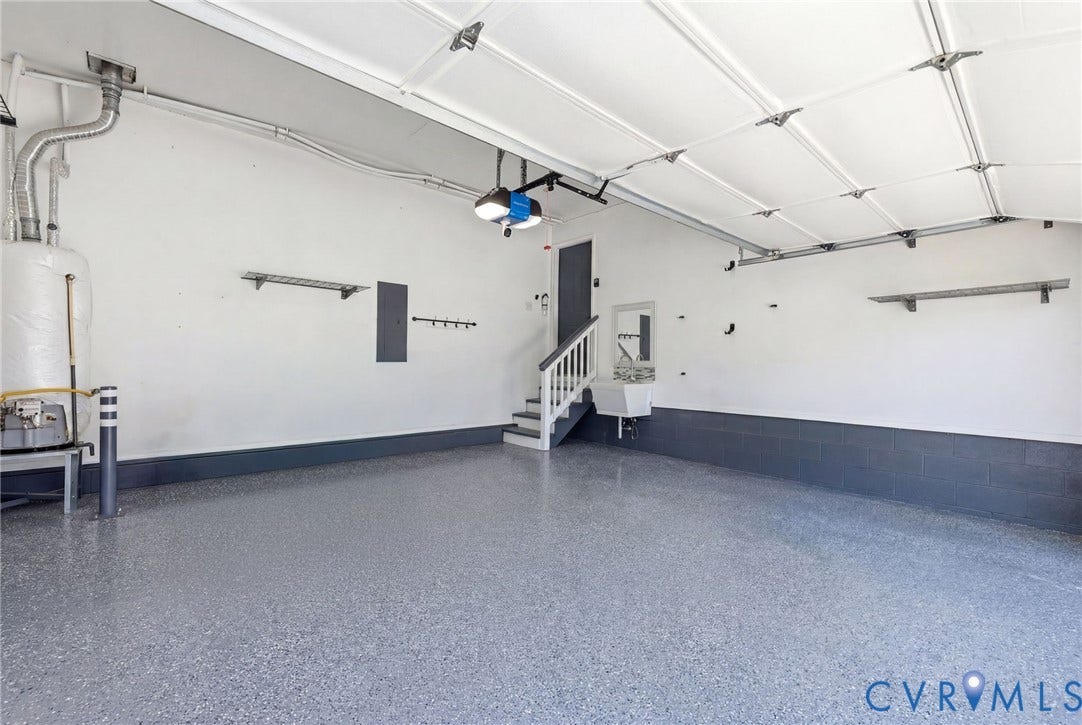 Spacious garage featuring a durable epoxy floor, white walls with a dark gray wainscoting, an integrated utility sink, and a staircase providing access to an upper level