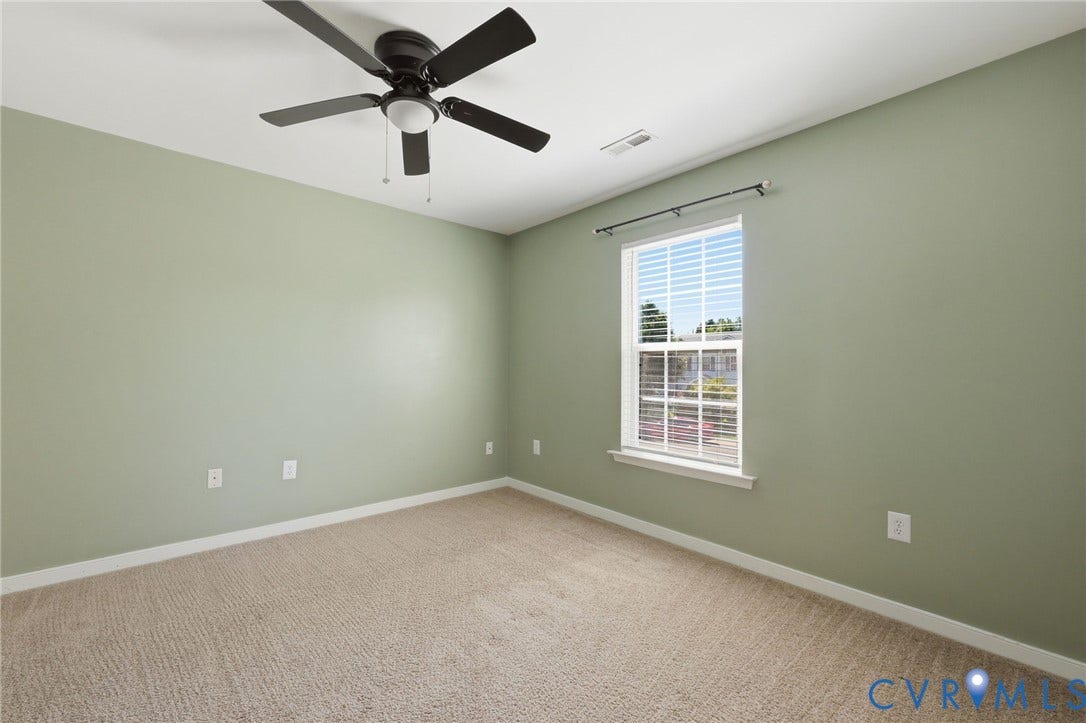 Bedroom featuring neutral green walls, carpeted flooring, a white-framed window with blinds, a dark-toned ceiling fan with integrated lighting, and white baseboards