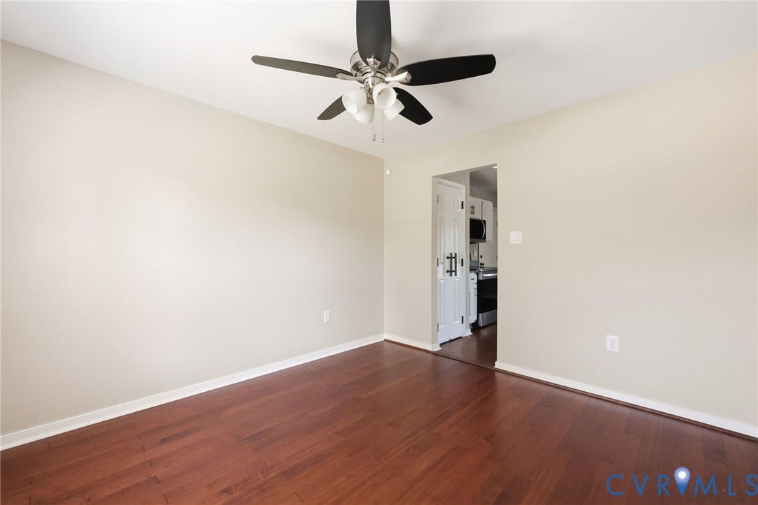 Spacious room featuring rich wood-finish flooring, light neutral wall paint, and a ceiling fan with integrated lighting