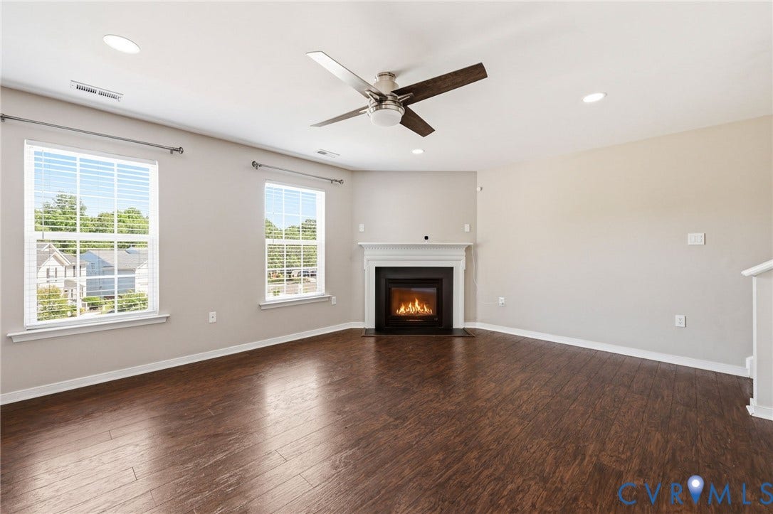 Living space featuring a corner fireplace with a white mantel, rich wood-finish flooring, and recessed lighting