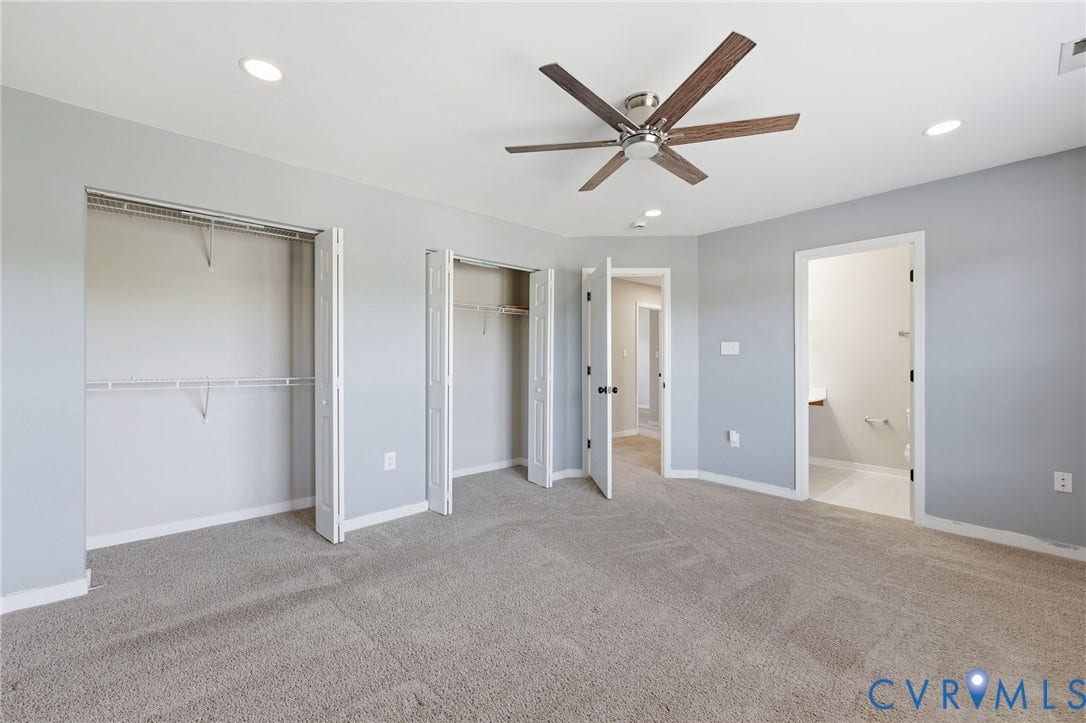 Spacious room featuring light gray wall paint, neutral-toned carpet flooring, and a modern ceiling fan with wood-finish blades