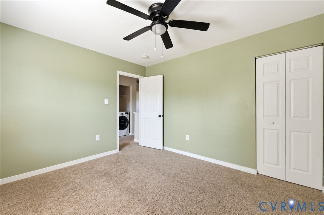 Spacious room featuring light green walls, brown carpeting, and a ceiling fan with black blades