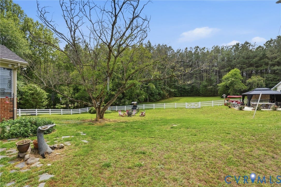 11016 Pridesville Road, Amelia, VA 23002 Expansive rear yard featuring a manicured lawn, white picket fencing, and mature perimeter trees
