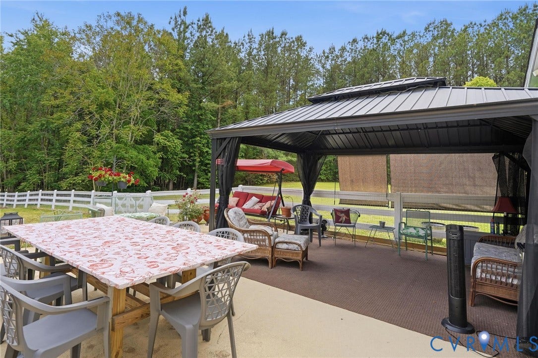 11016 Pridesville Road, Amelia, VA 23002 Expansive patio featuring a large metal gazebo with privacy screens, a white picket fence, and a backdrop of mature trees