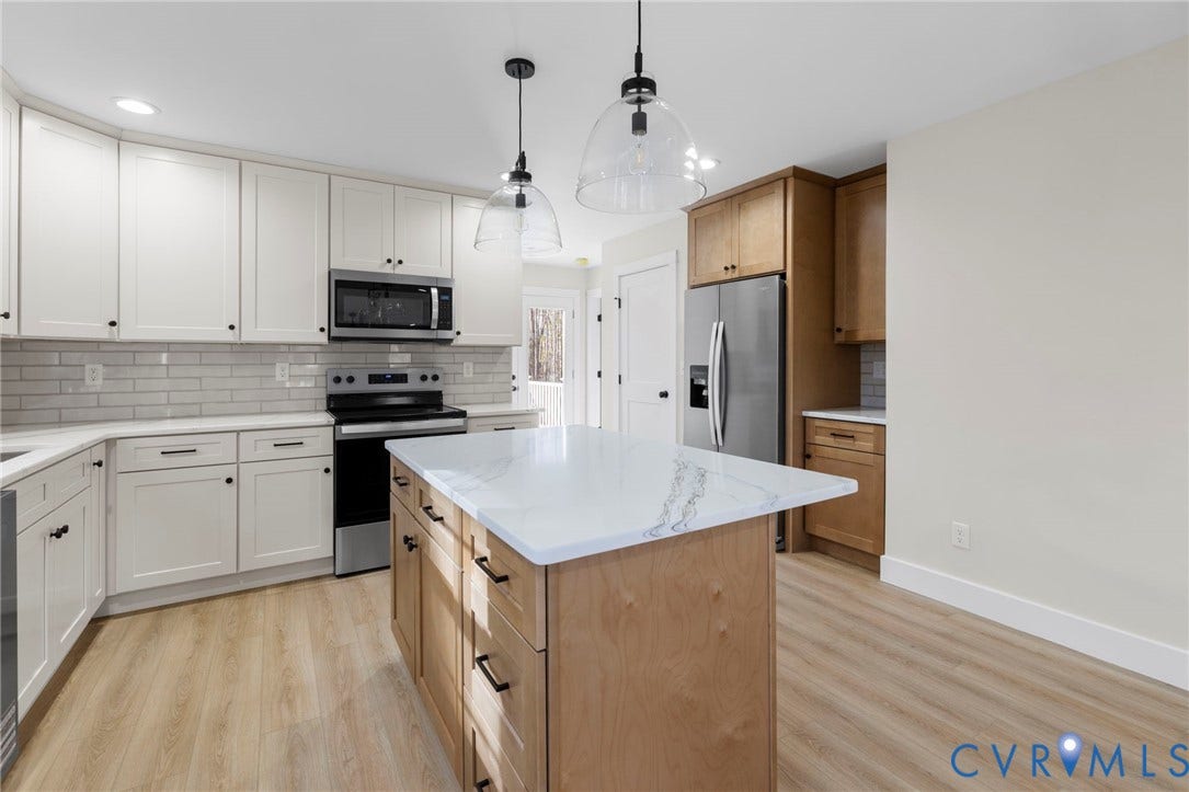 Modern kitchen featuring a central island with a white countertop, two-tone cabinetry, stainless steel appliances, subway tile backsplash, and light wood-finish flooring