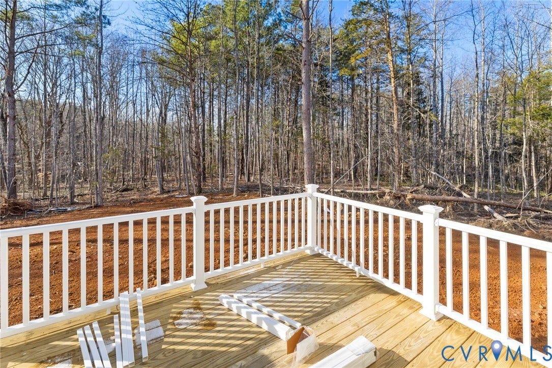 New construction deck featuring light wood decking and white railings, overlooking a wooded expanse with mature trees