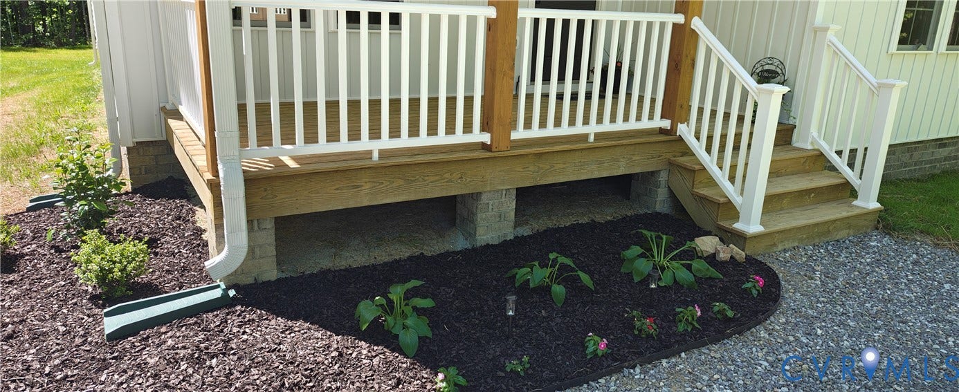 Wood-finish deck with white railing and steps, complemented by established landscaping beds, dark mulch, and a gravel pathway