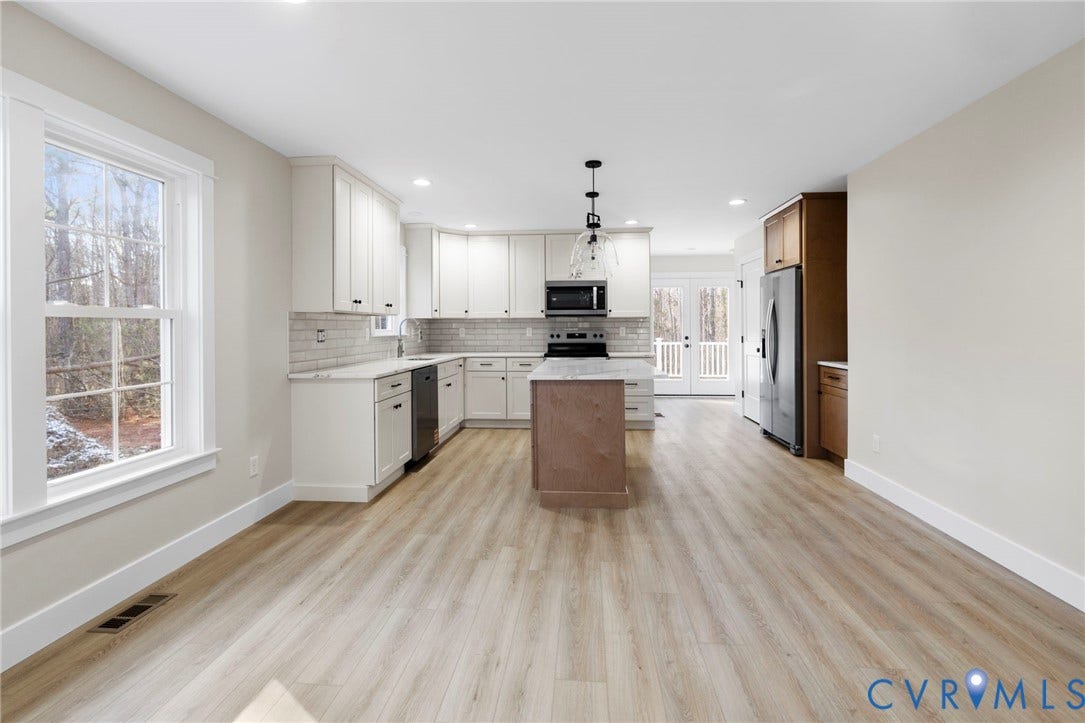 Open-concept kitchen featuring wood-finish flooring, white cabinetry with black hardware, a center island, and stainless steel appliances