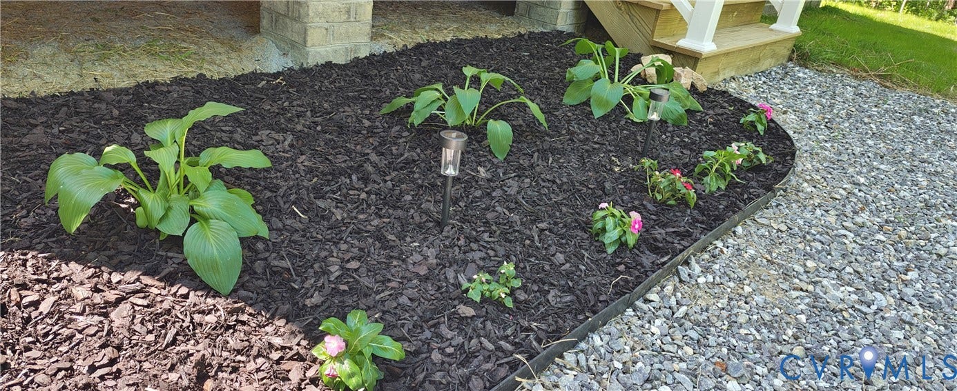 Landscaped garden bed featuring dark mulch, various plantings, and decorative solar lighting