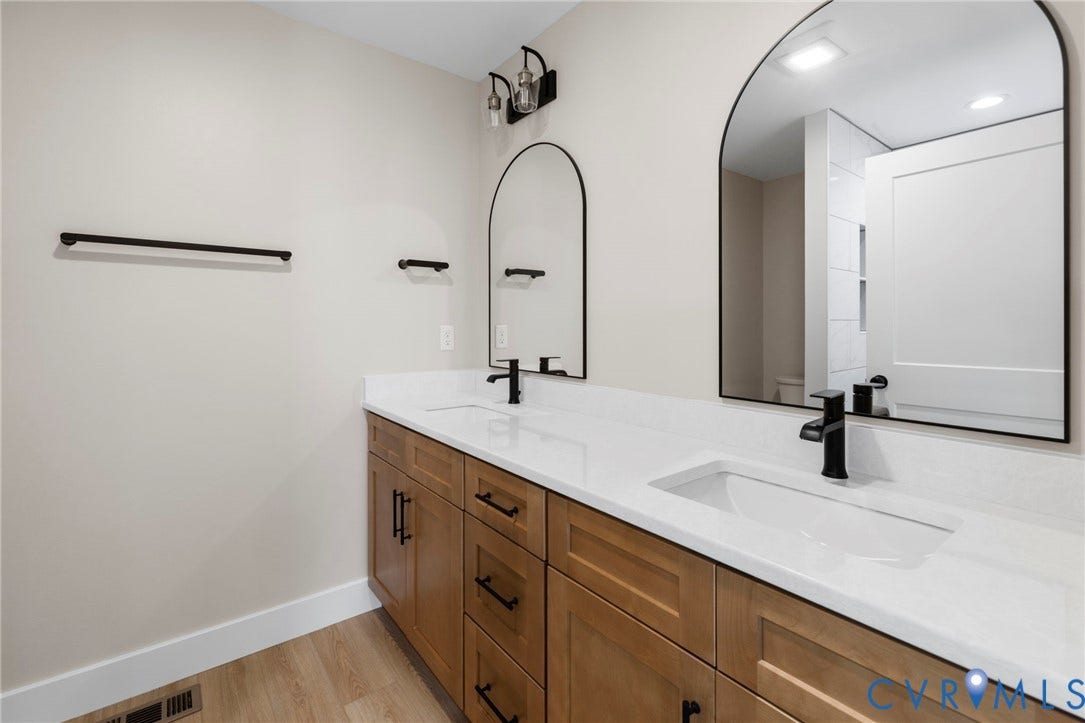 Dual vanity featuring wood-finish cabinetry, white countertops, and matte black hardware